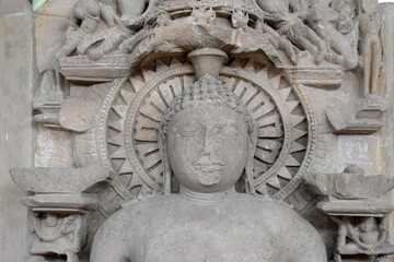 A finely detailed stone sculpture of a  Jain Tirthankara ADINATH,  with a serene expression, surrounded by ornate carvings 