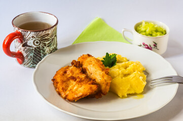 Fried schnitzel in breadcrumb with almonds, mashed potato on white plate, cup with lemonade,cucumber salad. - 763864442