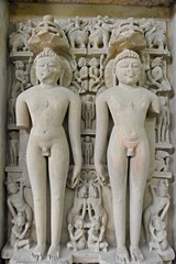 A finely detailed stone sculpture of a  Jain Tirthankara ADINATH,  with a serene expression, surrounded by ornate carvings 