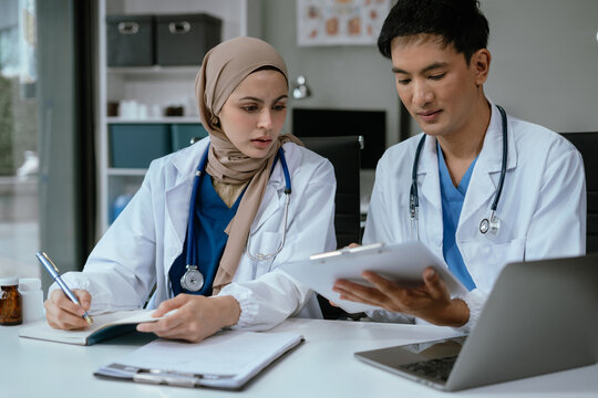 Pharmacist team writing making notes in drug information using laptop computer sitting at desk. Woman physician, nurse or pharmacist wearing white coat writing in paper notebook. - Powered by Adobe