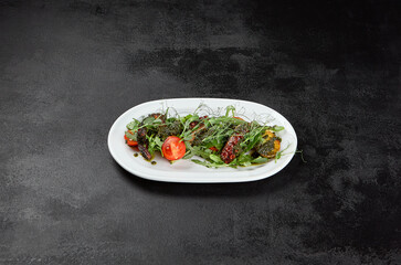 Salad with boiled octopus, potatoes and vegetables with pesto sauce on black stone background. Octopus salad with greens and potatoes in ceramic plate. 
