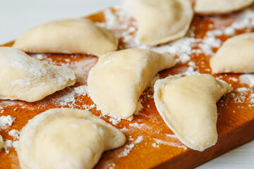 Close-up of handmade varenyky on a wooden board, view from above. Cooking dumplings on a wooden board.