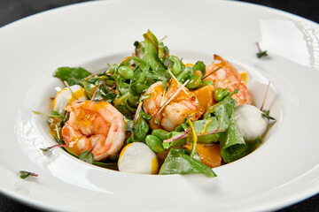 Healthy food - shrimp salad with mango, lettuce and mozzarella cheese on black background. Fresh salad with prawns and mango sauce. Seafood salad with cheese and mango on dark background.