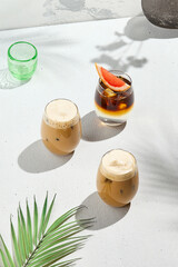 Assorted iced coffee on white concrete background with palm shadows. Minimal composition with cold summer drinks: espresso tonic, ice moccachino and latte. Summer composition for coffee menu.