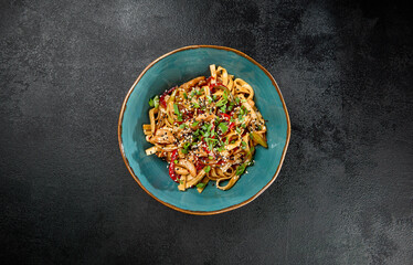 Traditional asian fried noodles with chicken and vegetables on dark background. Udon noodles with chicken on wok with sesame and green onion. Stir-fried udon with meat and vegetables on wok.