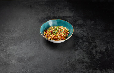 Traditional asian fried noodles with shrimp and vegetables on dark background. Udon noodles with prawns on wok with sesame and green onion. Stir-fried udon with seafood and vegetables on wok.