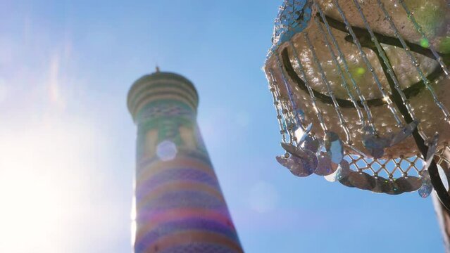A traditional headdress for women is sold on a street in the ancient city of Ichan Kala. A minaret covered with greenish-blue majolica can be seen in the background. Khiva, Uzbekistan