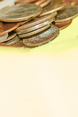 A pile of old and worn coins are stacked on a bright yellow surface, showing details of the texture and the rusted color.