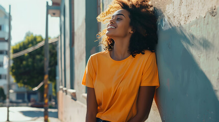striking mockup featuring a black happy woman in an orange t-shirt standing on a vibrant city street, exuding confidence and urban style. blue wall - obrazy, fototapety, plakaty