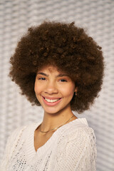 A woman with curly hair is smiling and wearing a white sweater