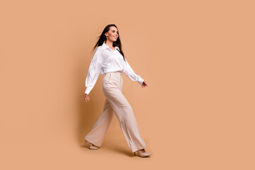 Fototapeta na wymiar Full length photo of sweet adorable lady dressed white shirt walking heels looking empty space isolated beige color background