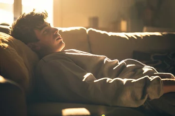Deurstickers young man in sweats lying on couch, backlit with daylight © altitudevisual