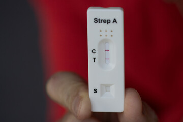Close-up of hand holding positive streptococcus test during infection, diagnostic test done at home...