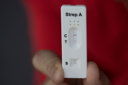 Close-up of hand holding positive streptococcus test during infection, diagnostic test done at home for telephone consultation with doctor.