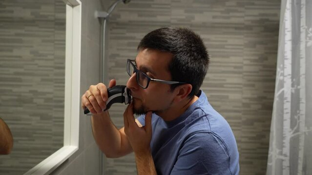 Married man in glasses shaving beard in bathroom, checking progress