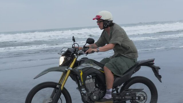 Man rides enduro motorcycle on sandy ocean beach in sunset 