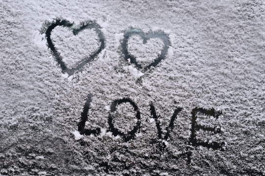 the word love and two hearts on a snow covered glass. concept