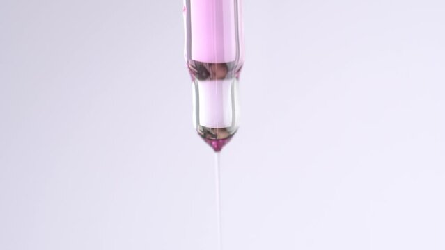Close up of pipette with pink cuticle oil. Drops of essential oil or serum fall from a glass pipette, macro.