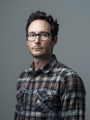 Obraz premium A portrait of a man with styled hair, glasses, and a neutral-looking plaid shirt