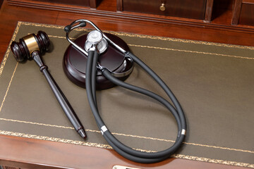 A close-up of a judge's gavel and a black stethoscope on top of a legal book, signifying the...