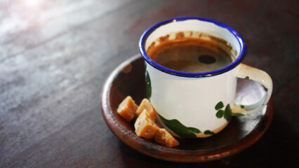 A cup of black coffee with brown sugar on ceramic plate on the wooden table. Morning with...