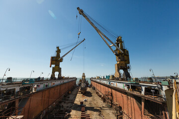 Ship repair dock with towering cranes, industrial setting under clear sky. Maritime vessel...