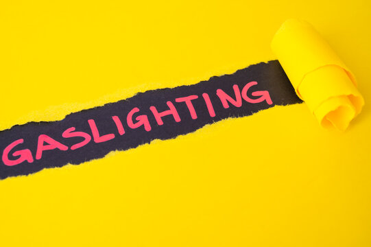Black surface, with word gaslighting in red. Underneath torn yellow cardboard.
