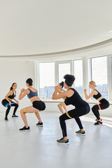 group of diverse women in sportswear looking at trainer and squatting with resistance bands
