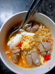Close-up of the delicious instant noodle soup mixed with meatballs, boiled egg and sliced red chili peppers in a bowl ready to eat.