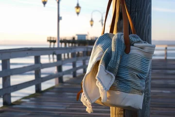 Selbstklebende Fototapeten beach bag with a cozy blanket for a chilly evening walk on the pier © altitudevisual