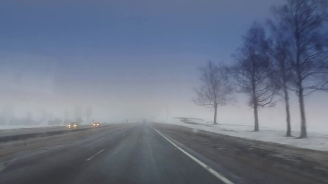 View from the windshield of a car on the road in winter in bad weather with fog and poor visibility. Encountered cars with headlights on. Snowy roadsides. Copy space for text