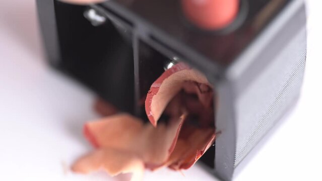 Nude beige cosmetic pencil rotates in black dual makeup pencil sharpener, macro. Sharpening lip pencil with sharpener tool on white background