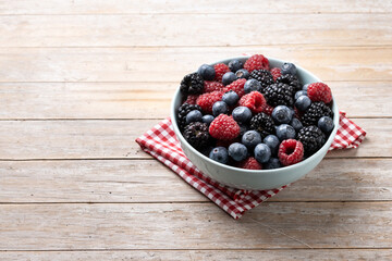 Fresh assortment berries in bowl on wooden table. Copy space