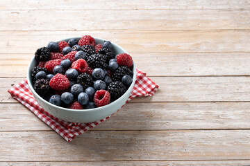 Fresh assortment berries in bowl on wooden table. Copy space