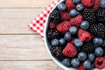 Fresh assortment berries in bowl on wooden table. Top view. Copy space