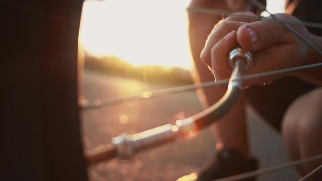 Close up cyclist inflates flat tire by compact hand pump with retractable hose with Schrader inflator chuck connector for valve stem at sunset, punctured wheel, broken bicycle out of town outside city