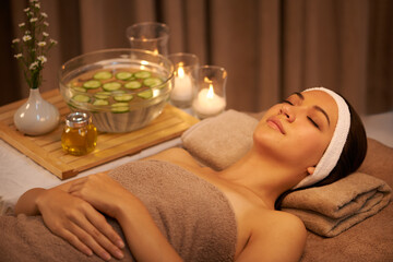 Sleeping, relax and woman at massage table in spa with cucumber for peace, calm or skincare. Body, salon and person resting for aromatherapy with candles for natural beauty or health with eyes closed