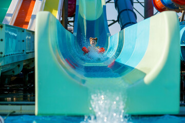 Little preschool girl on water slide in aqua park. Happy child having fun on water slides on family summer vacation in tropical resort. Amusement park with wet playground for young child and baby.