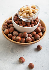 Bowls with peeled and whole healthy hazelnut nuts on light table.Macro.