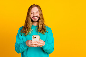 Photo of cheerful man beaming smile hold smart phone empty space isolated on yellow color background