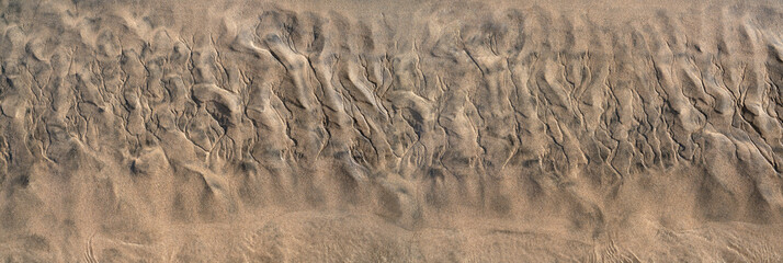 Abstrakte Struktur im braunen Sand am Strand bei Ebbe, unten das noch vorhandene Flachwasser - Panorama Nahaufnahme