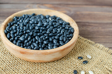 Raw black bens in a wooden bowl on burlap on a wooden table. Rural style. Vegetarian food concept. Horizontal orientation. Selective focus.