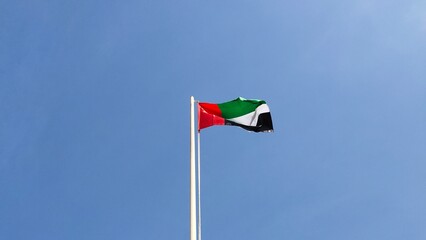 UAE country national flag hanging and flying crinkled high on a flagpole with a blue sky background. The United Arab Emirates Flag Day celebration concept. Flag wave during wind spectacular view.