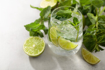 Mojito with ice, lime, and mint on a white stone table.