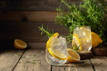 Cocktail gin tonic with ice, lemon, and rosemary on a old wooden table.