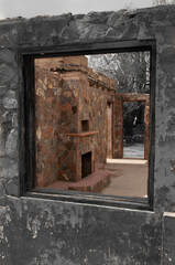 Peering through a decaying stone window frame to a deserted old building with a clear sky