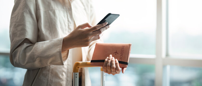 Tourist woman using mobile smartphone and holding passport with suitcase traveling between waits for flight in Airport Terminal, flight check in, Tourist journey trip concept