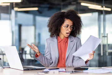 Confused African American businesswoman reading papers with a shocked expression in a modern office...