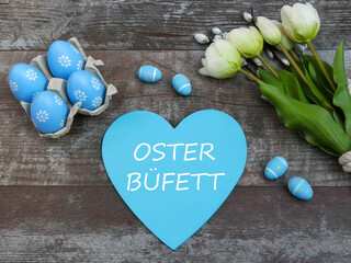 Der Text Osterbüfett ist auf ein Herz geschrieben mit Ostereiern und Blumen dekoriert..	