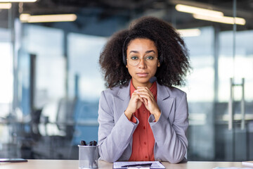 A professional woman sits at her desk in a modern office, hands clasped, deep in thought amidst a...